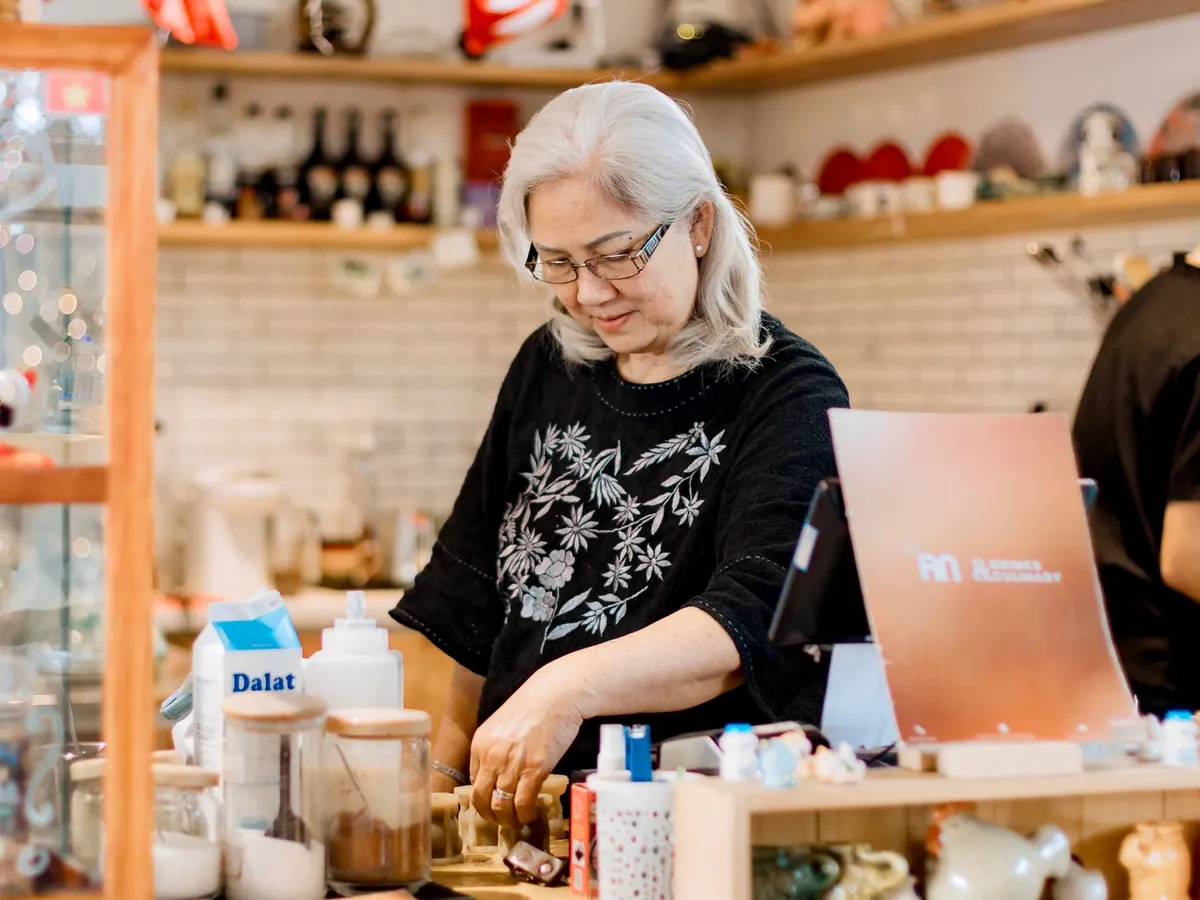 Senior woman working behind the counter in a cozy, warmly lit coffee shop.