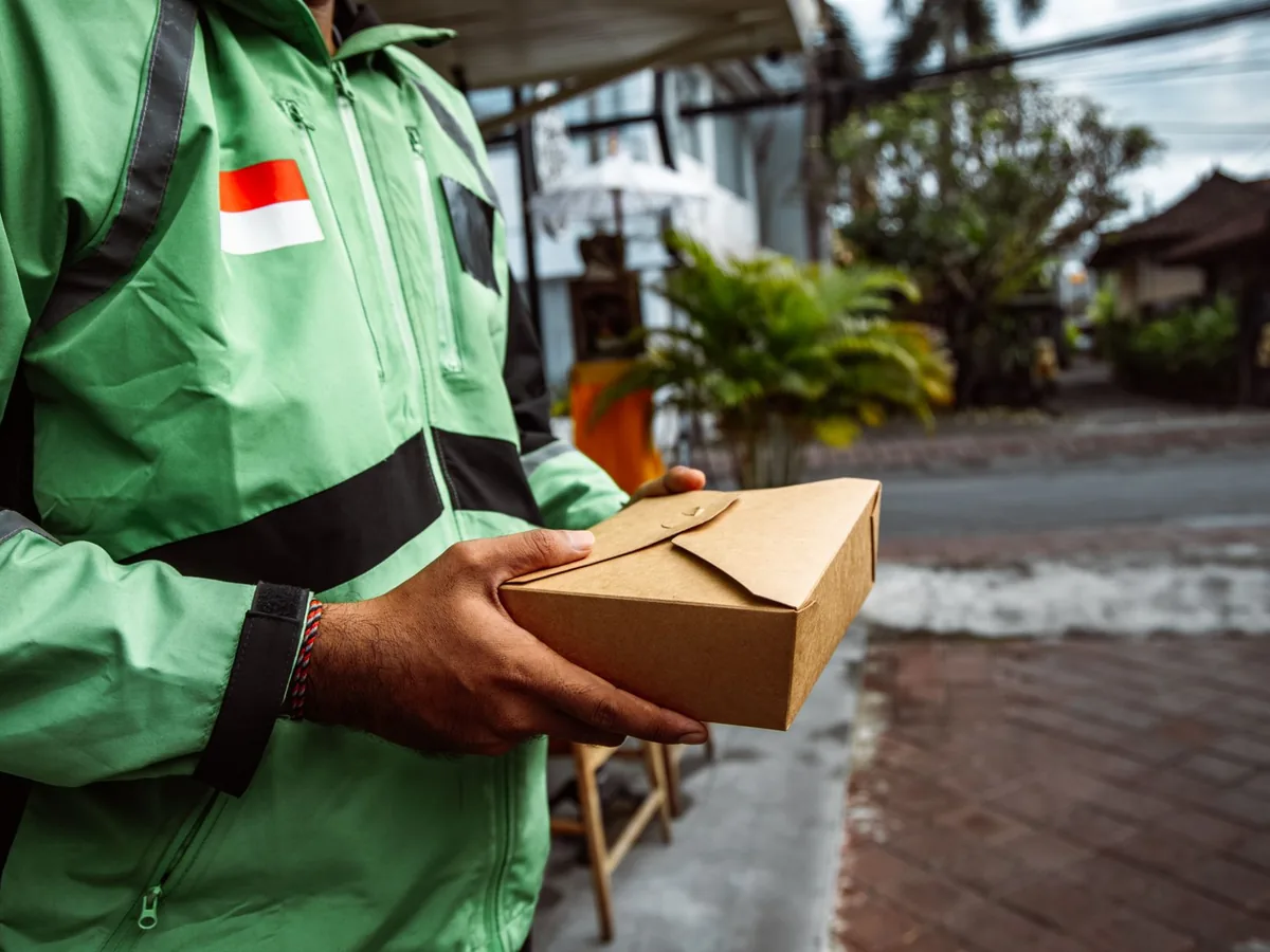 A courier in a green jacket delivers a food box.