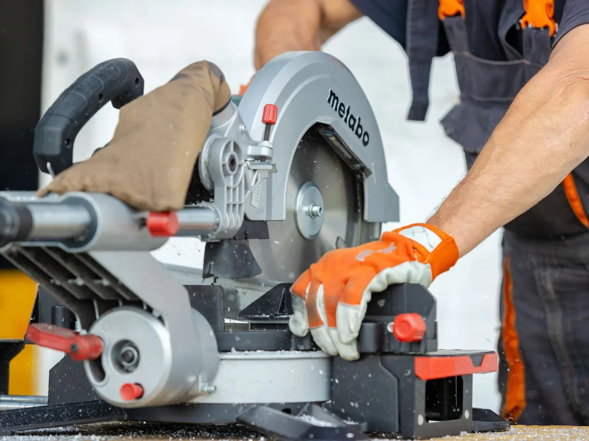 A worker cuts a metal beam with a powered saw.