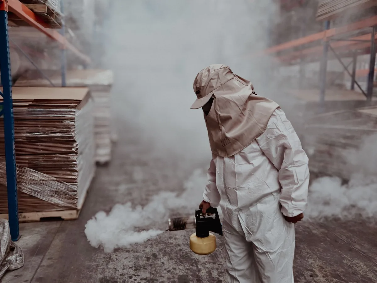 A pest control technician uses fogging equipment inside a warehouse.
