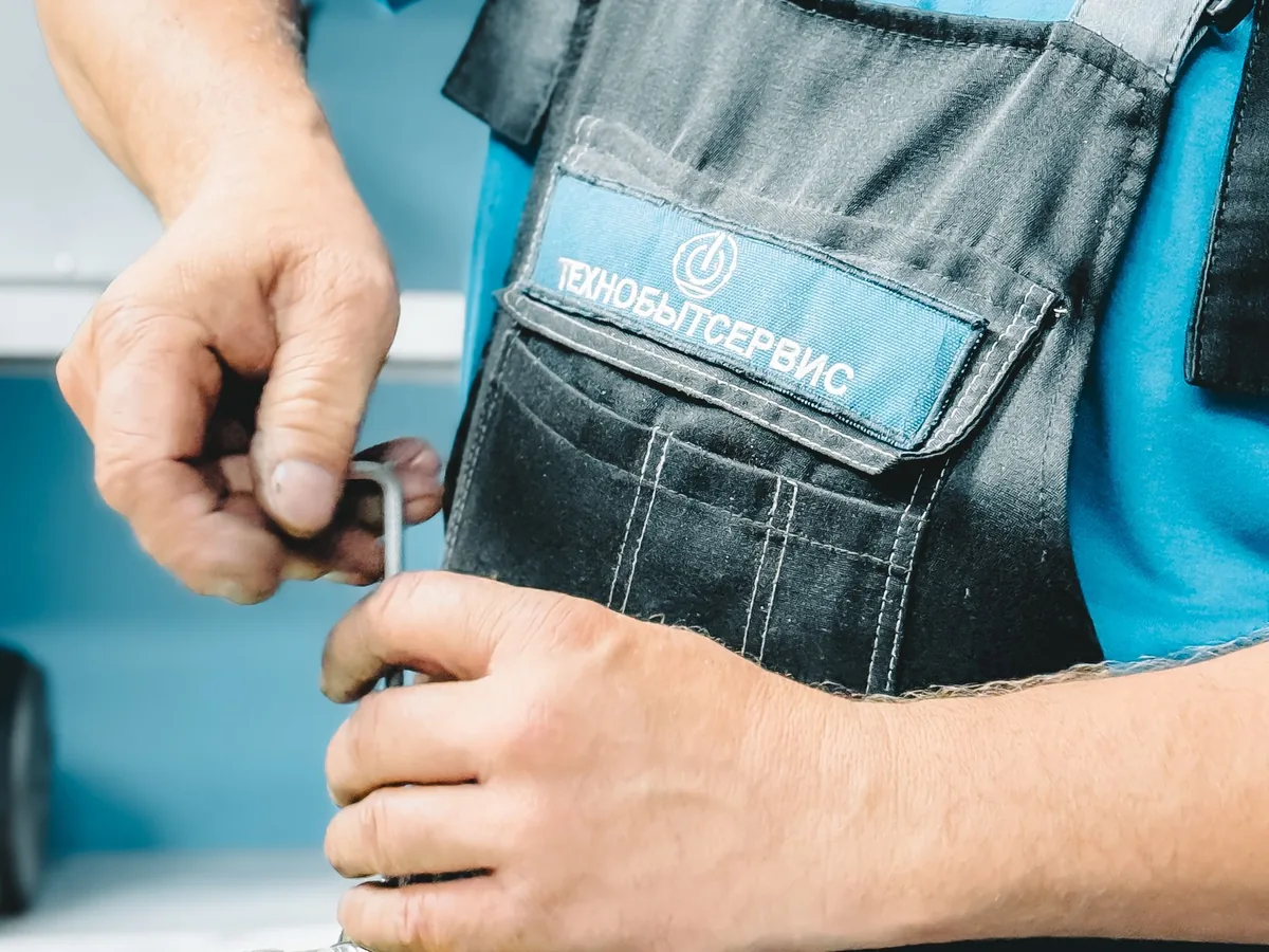 A plumber works on a metal pipe fitting indoors.