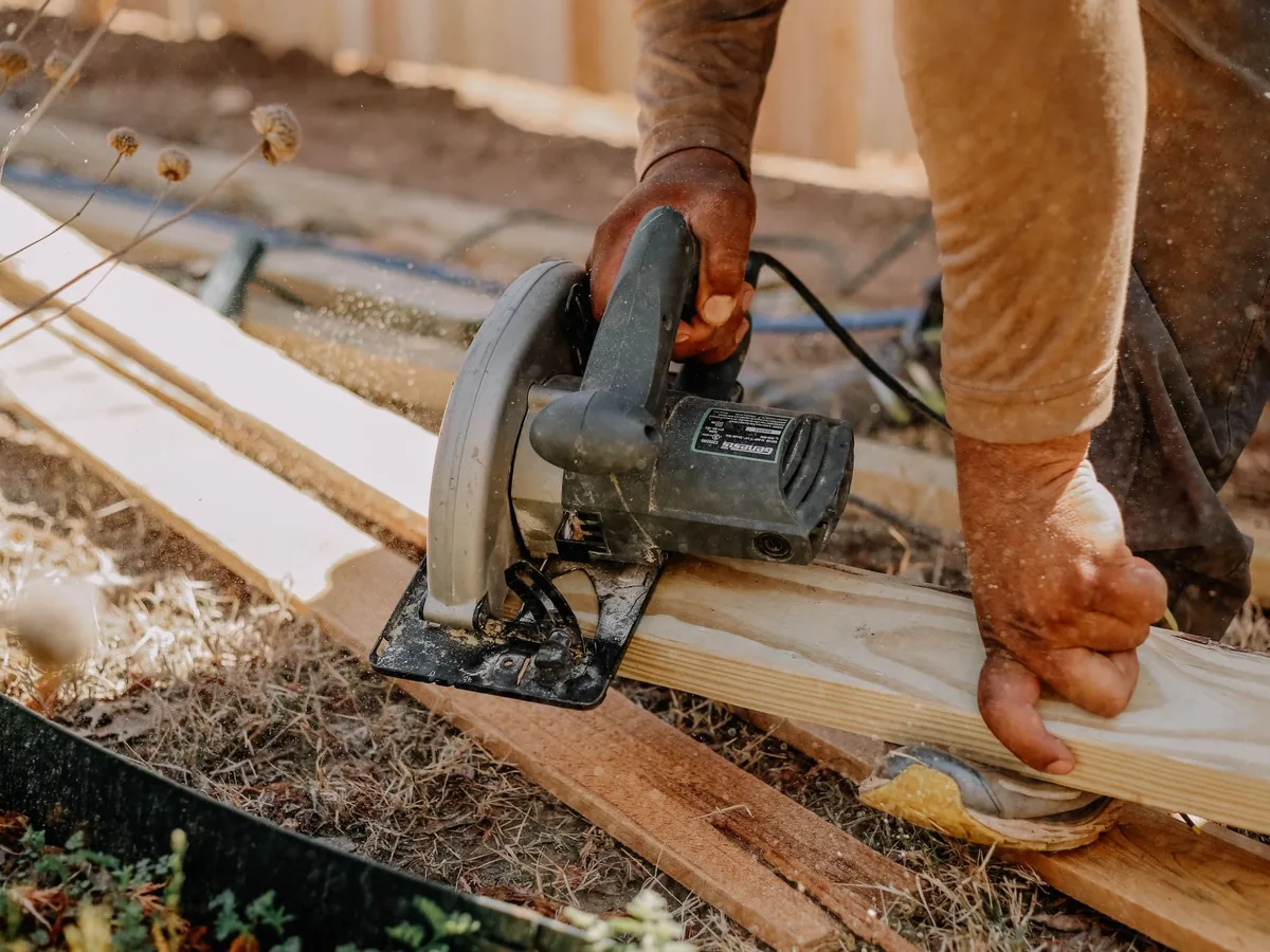 A carpenter uses a circular saw at an outdoor workbench.