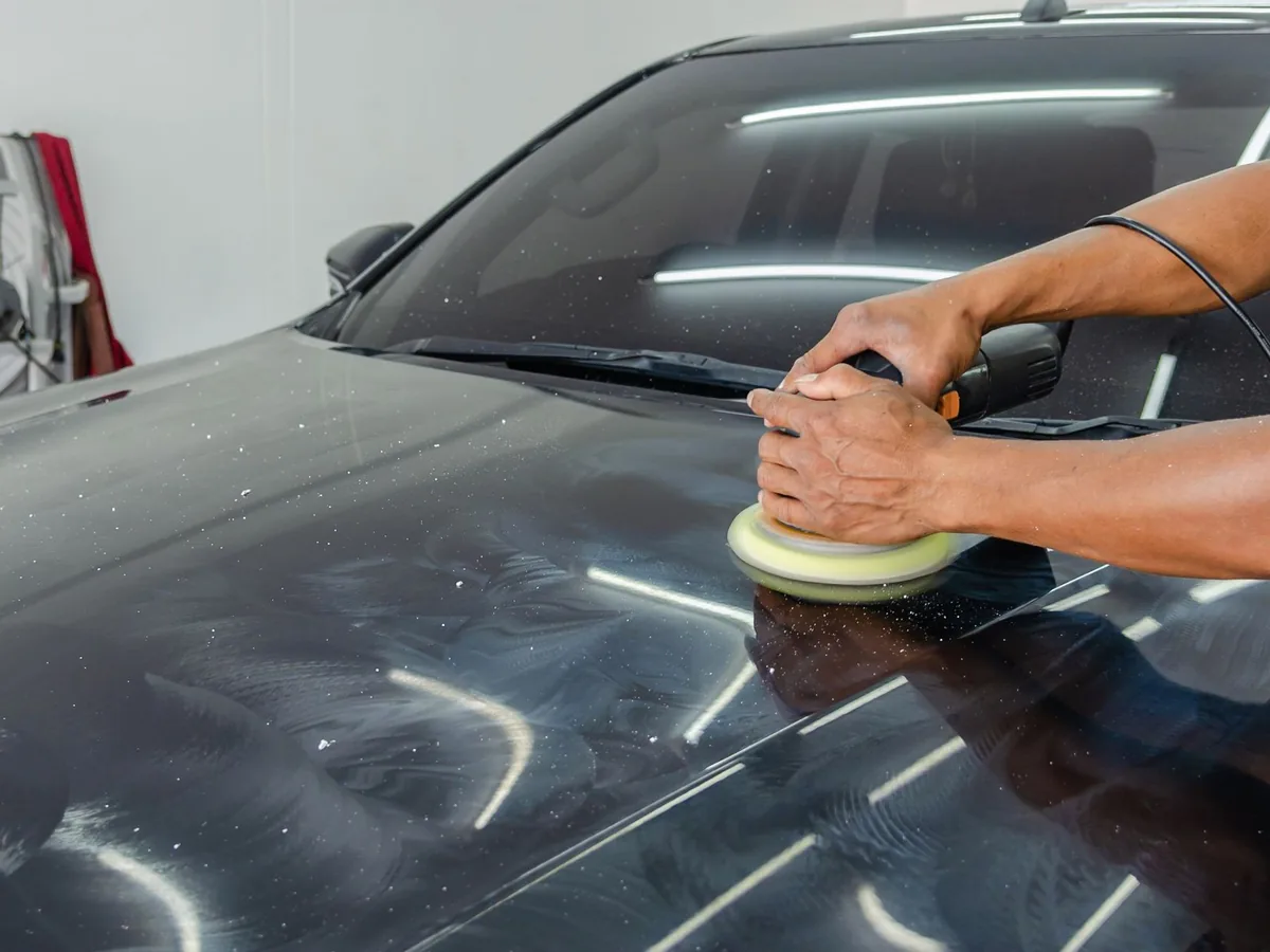 A detailer polishes a black car with an electric buffer.