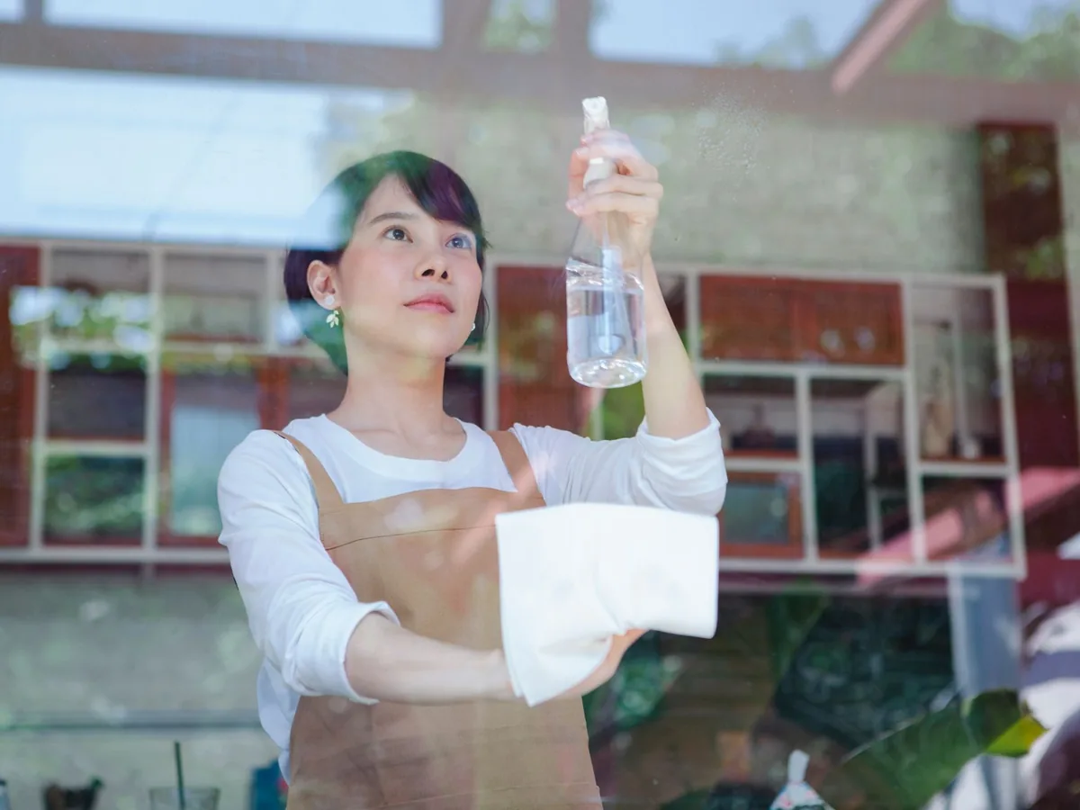 A cleaner in a brown apron wipes a window.