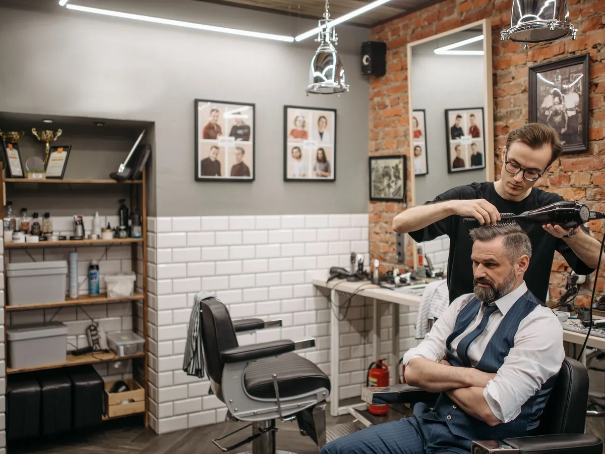 A barber blow-dries a customer’s hair.