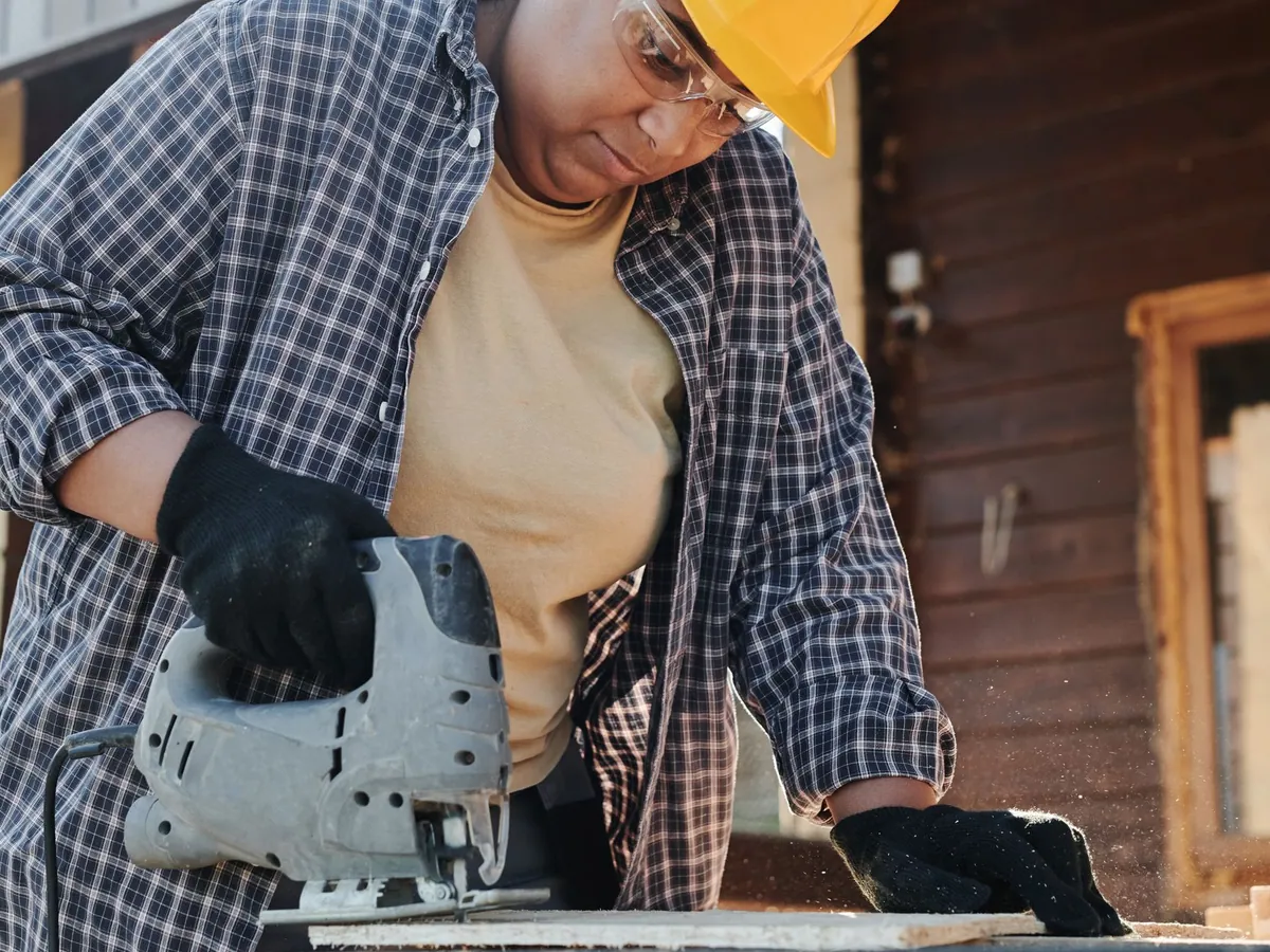 A focused construction worker using an electric jigsaw on wood outdoors.